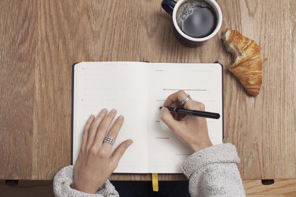 Hand writing in a notebook next to a coffee