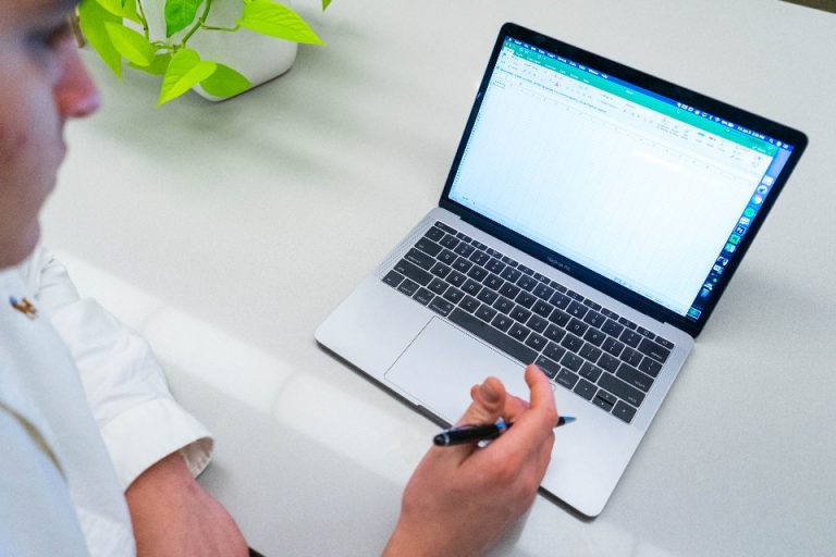 Person taking notes beside an open laptop